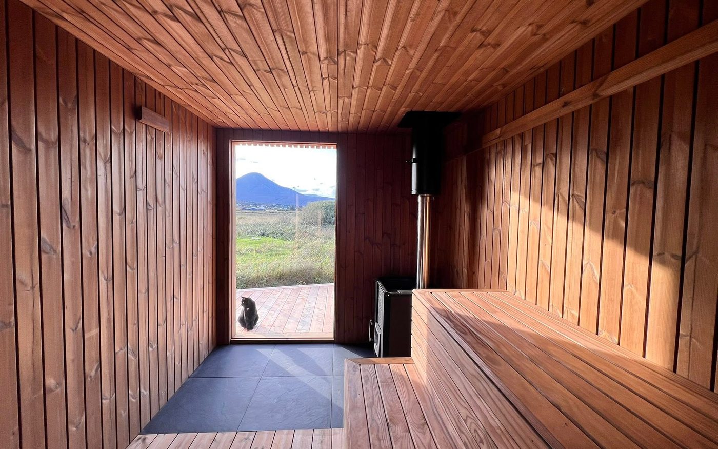 Inside a DK-built sauna, looking out through the glass door over a mountain landscape
