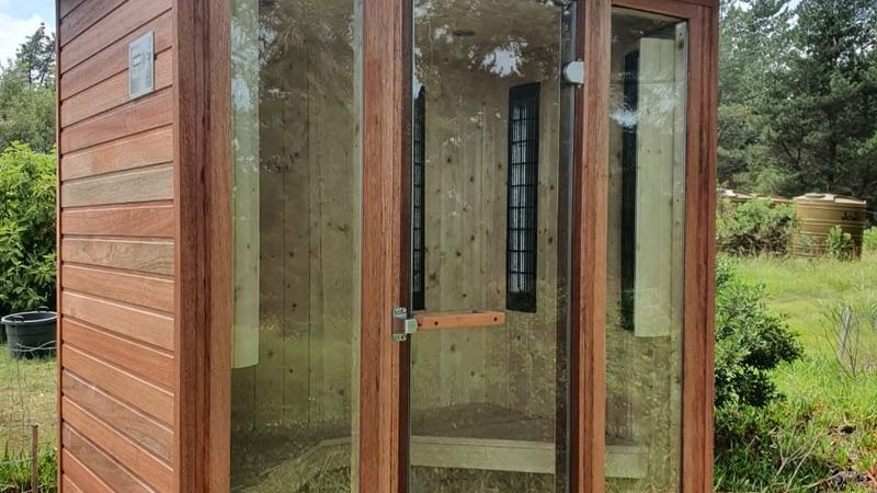 Cedar-clad garden sauna cabin with full glass front standing on a wooden deck