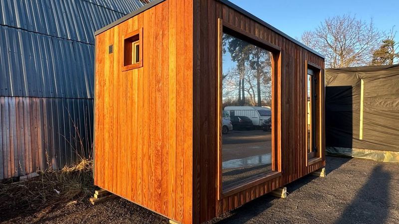 Outdoor cedar sauna cabin with a large picture window glowing in golden sunlight