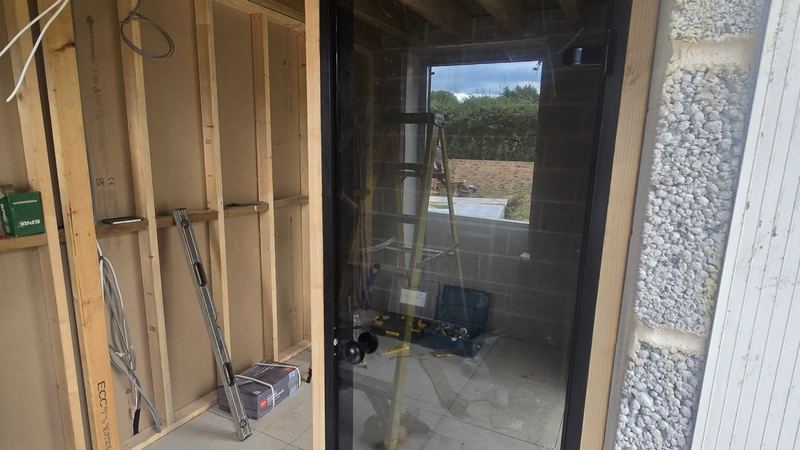 Sauna construction in progress with timber framing, cables and a fitted glass door