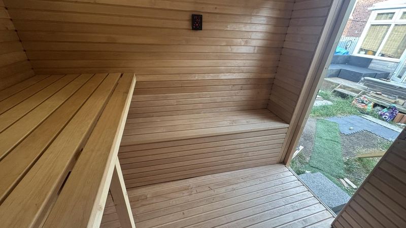 Finished light-wood sauna interior with benches and a wall-mounted digital controller