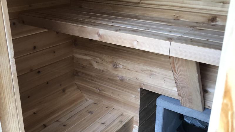 Natural wood sauna with tiered benches and a heater recess built beneath the top bench