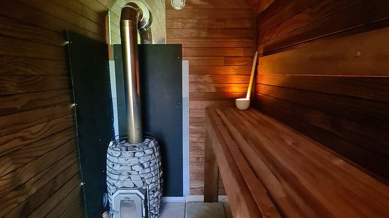 Wood-fired sauna heater with stainless flue inside a dark cedar sauna interior