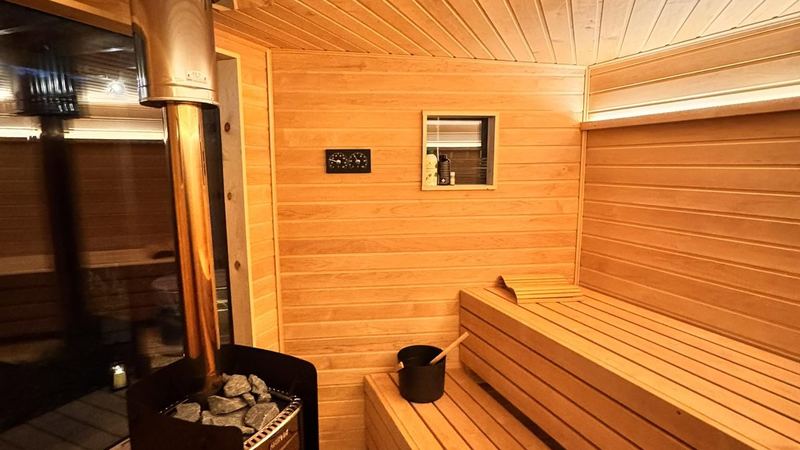 Sauna interior glowing warm orange at first firing with a bucket and ladle on the bench