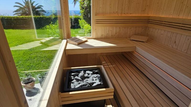 Bright sauna interior with a large window overlooking a lawn, palms and the sea