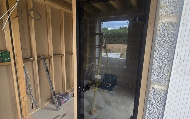 Sauna build in progress: timber framing with a fitted glass door and first-fix wiring